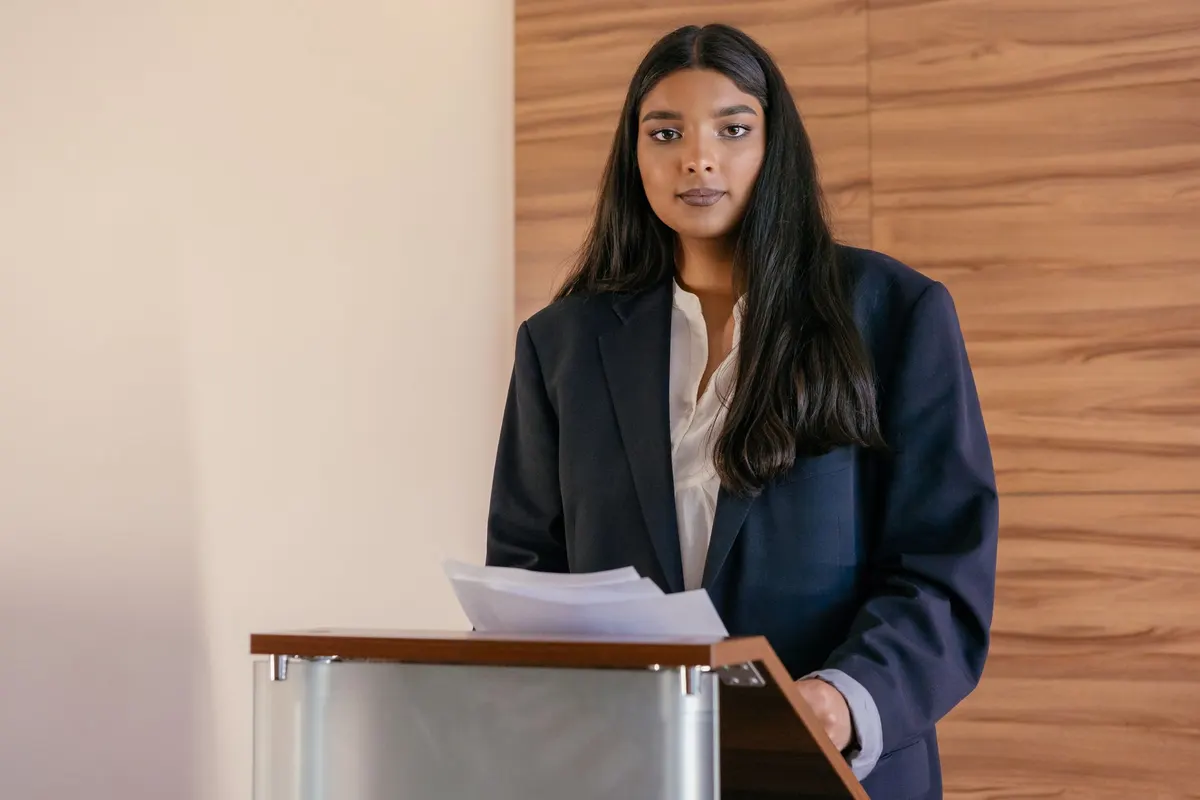 A young woman in a navy suit speaking at a lectern
