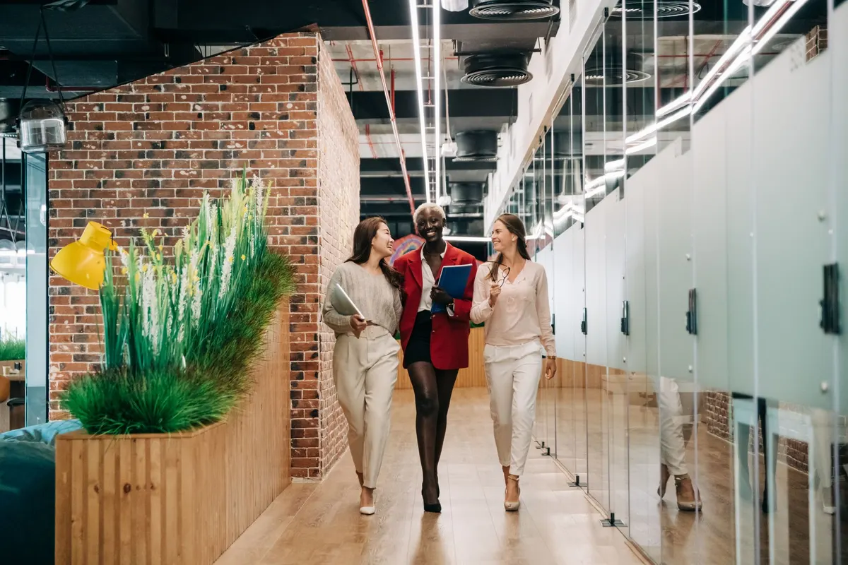 Three colleagues walking and talking down a bright office corridor