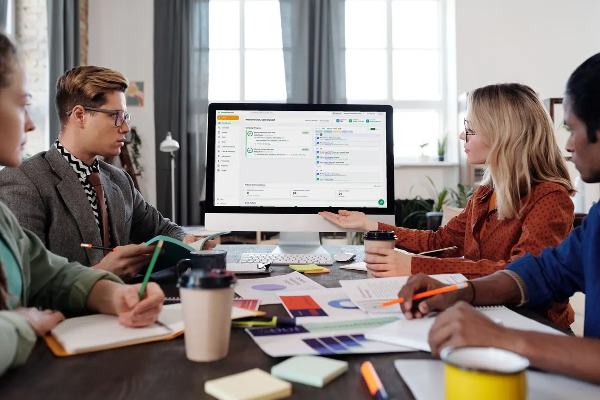 A team at a meeting table reviewing the FundraiserMax analytics dashboard on a shared monitor