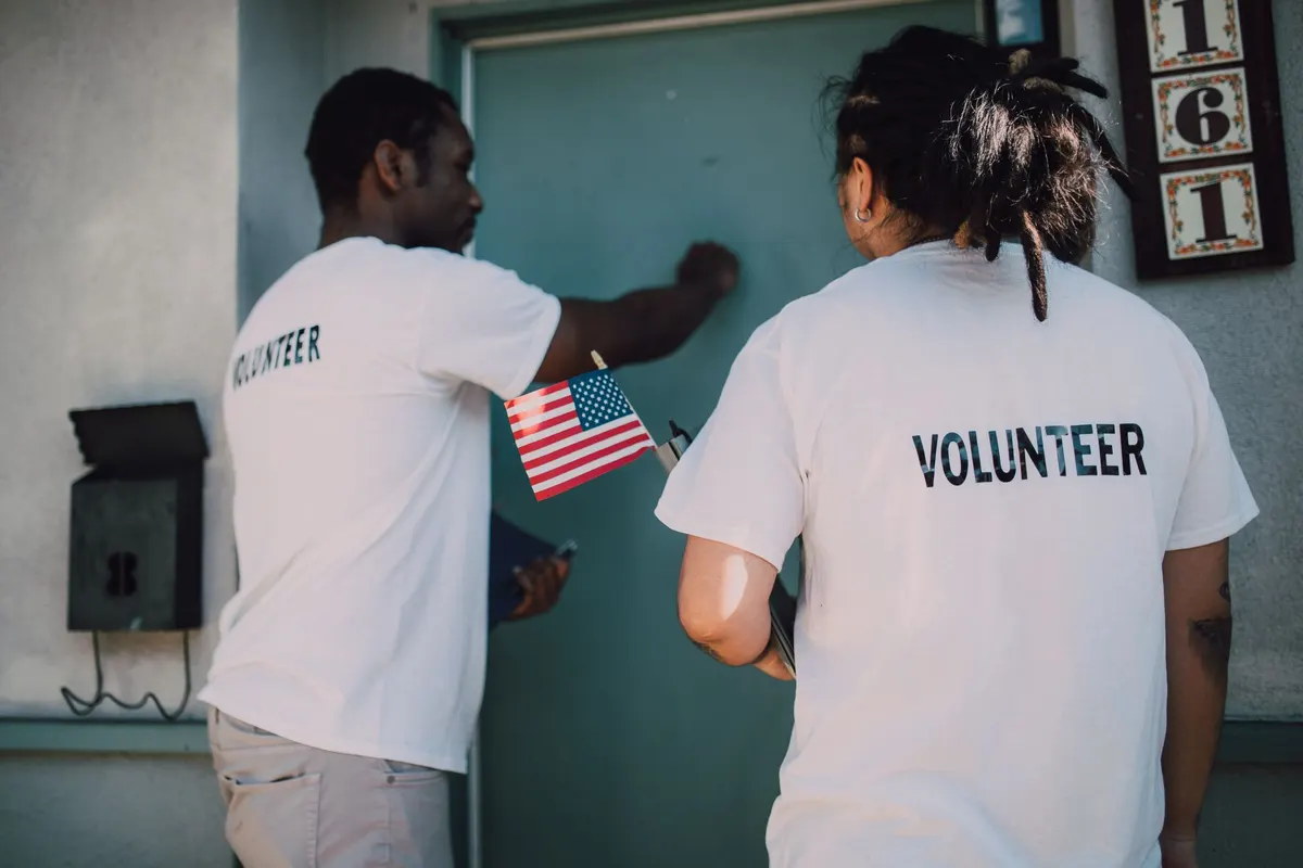 Two volunteers in volunteer shirts knocking on a front door
