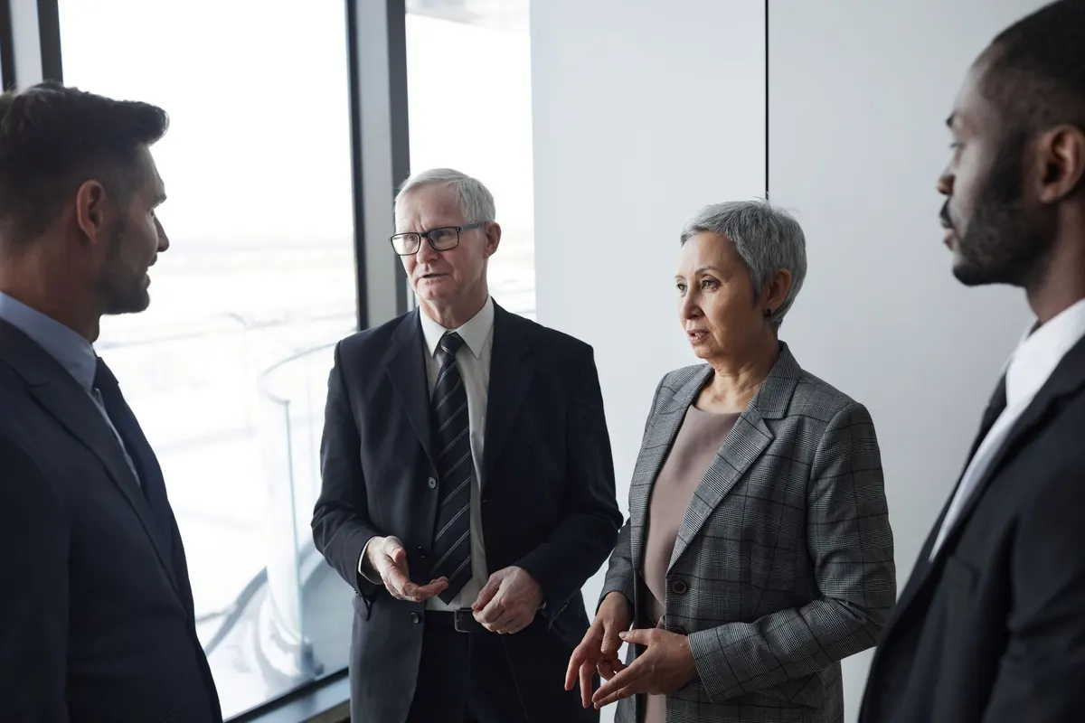 Four people in suits talking beside a tall office window